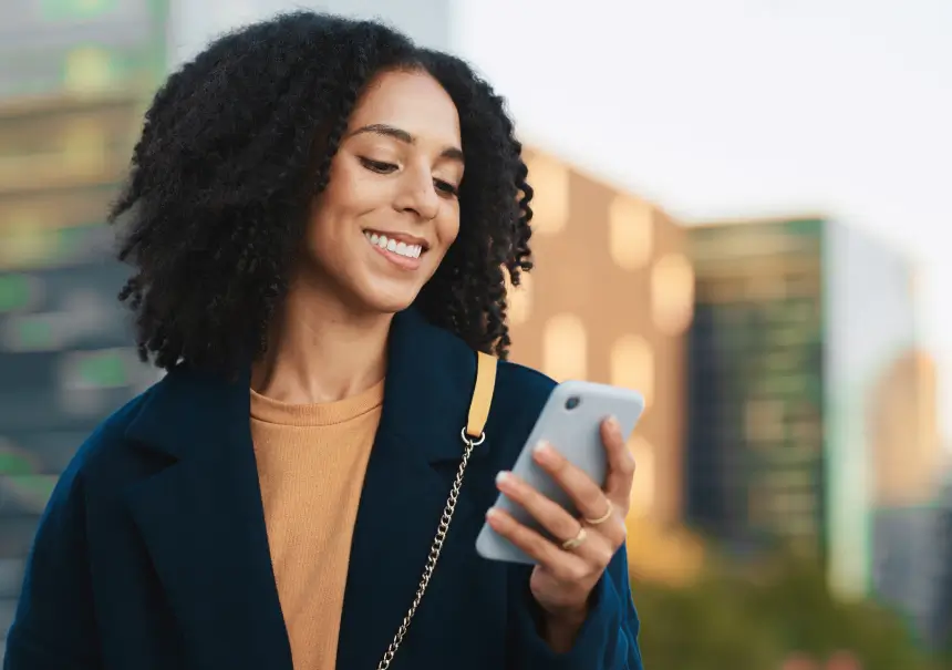Una donna sorridente che controlla le notifiche sul suo smartphone, rappresentando l'uso strategico di WhatsApp e Mobile Push per ottimizzare il funnel di vendita nell'e-commerce.